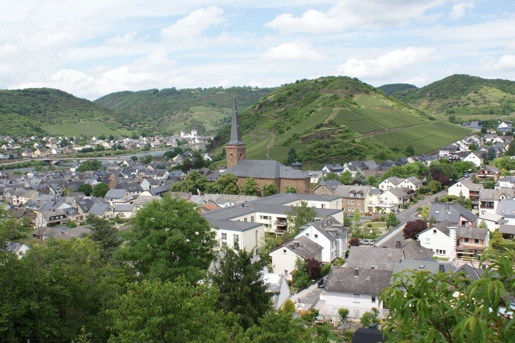 Une ville où se dresse une église imposante, entourée de bâtiments résidentiels et de collines verdoyantes.