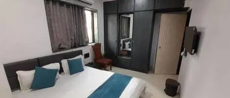 A hotel room with a bed, a ceiling fan, an air conditioning unit, a wardrobe, and a television.