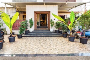Entrada de un edificio con escalones que conducen a una puerta, rodeada de plantas en macetas.