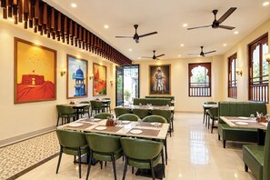 Un restaurant amb diverses taules i cadires, ventiladors al sostre i obra d'art a les parets.