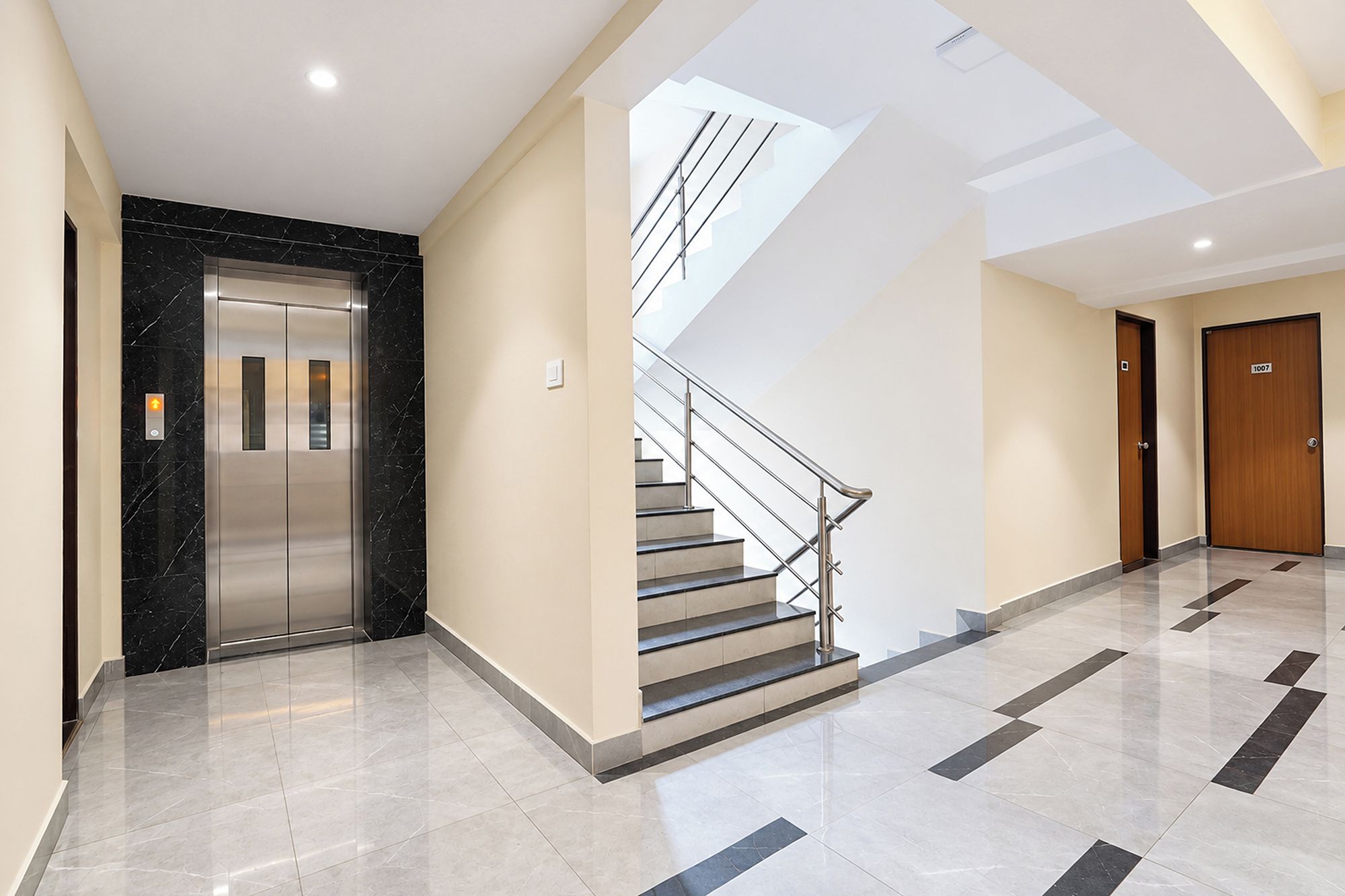 A modern interior with a marble elevator, a staircase with metal railings, and a hallway leading to a door marked '1007'.