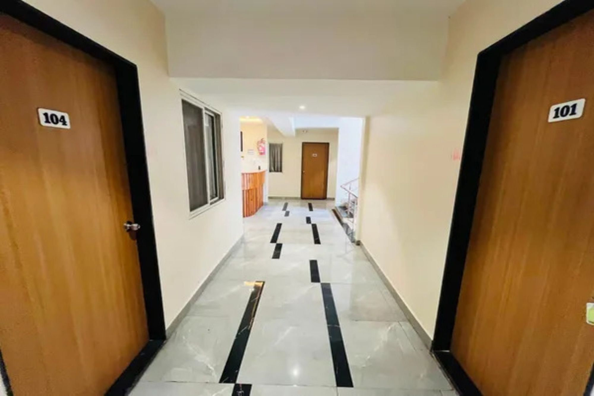 A hotel corridor with doors numbered 104 and 101, leading to a room with a window and a door.