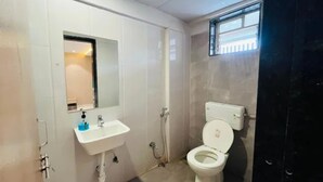 Un baño con lavamanos blanco, un espejo, inodoro y zona de ducha.