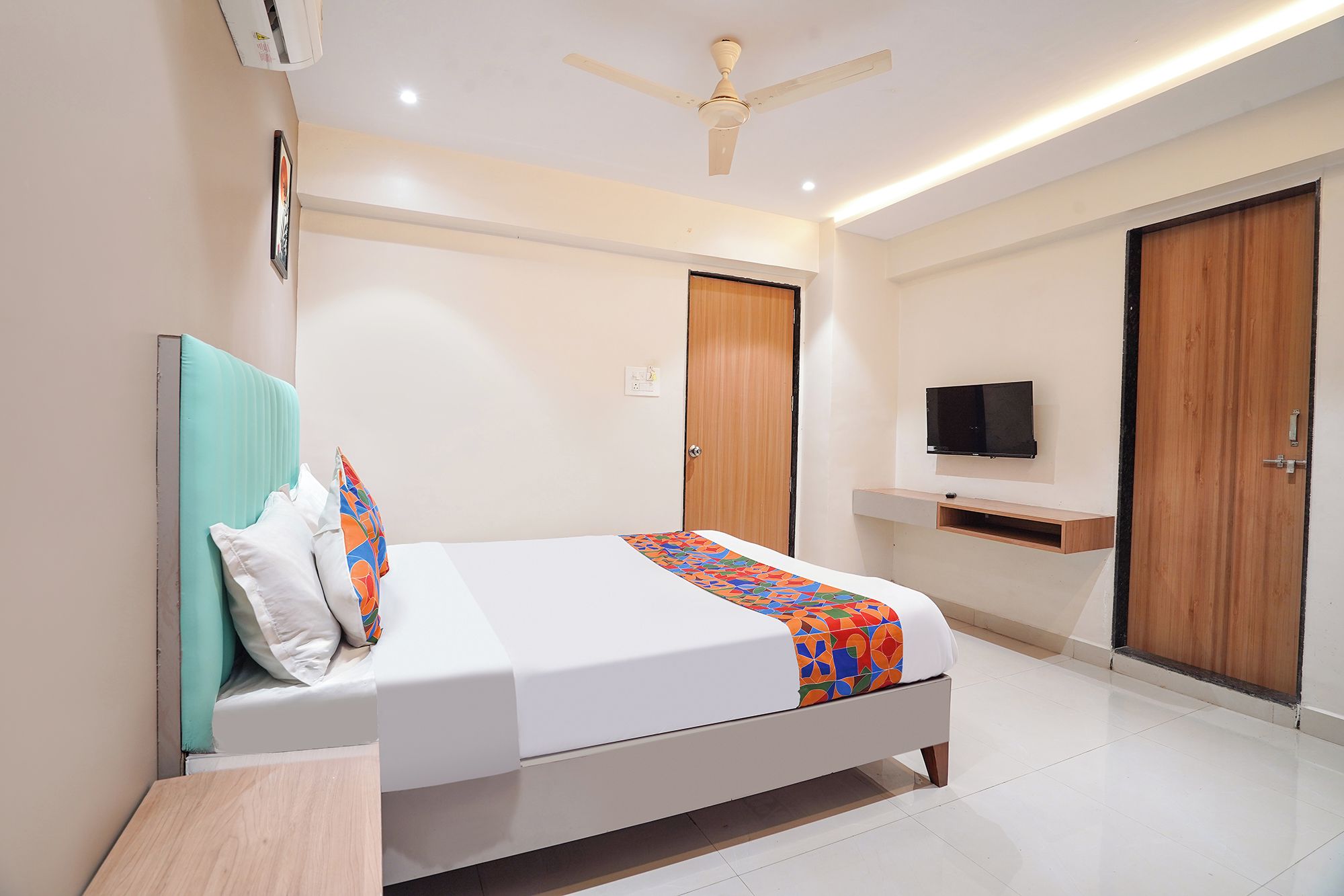 Une chambre à coucher moderne avec un lit, un ventilateur de plafond, un téléviseur fixé au mur et une porte en bois.