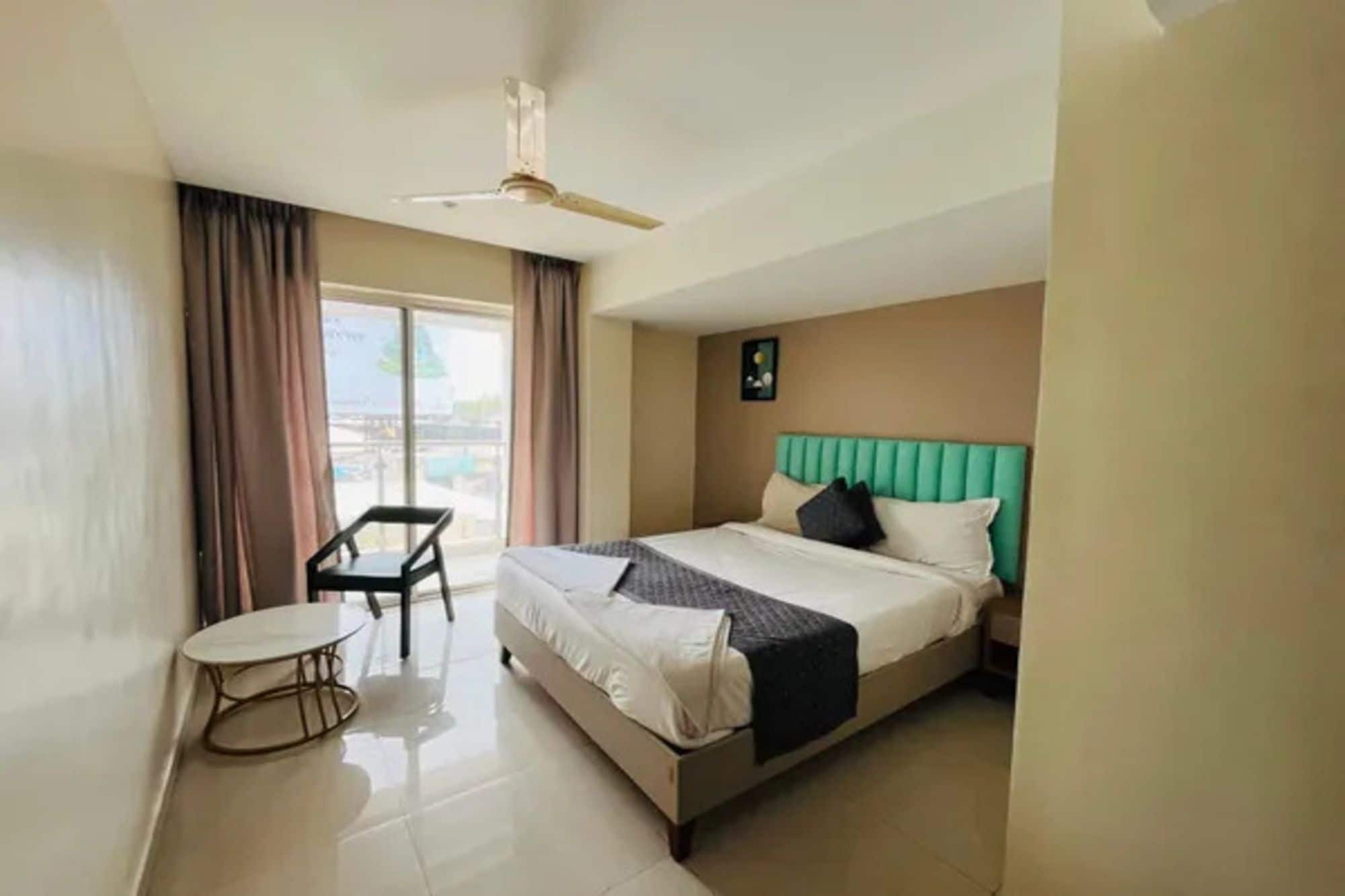 A hotel room with a bed, a small table, a chair, and a ceiling fan.