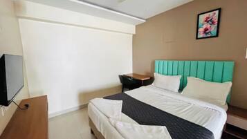 A hotel room with a bed, a television, a desk, and a ceiling fan.