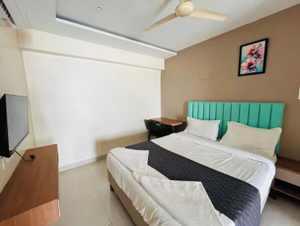 A hotel room with a bed, a television, a desk, and a ceiling fan.