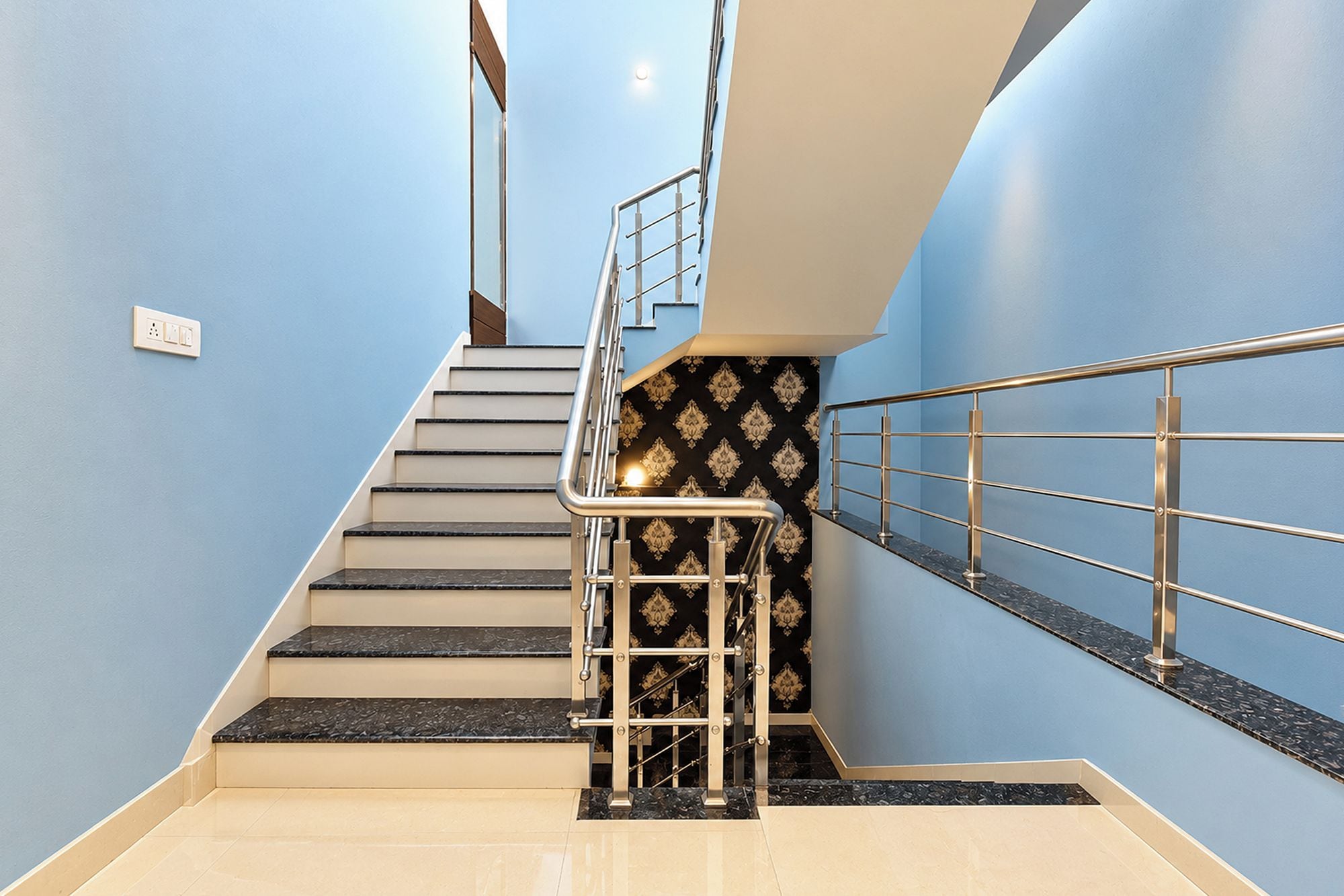 A staircase with a metal handrail and a patterned wall.