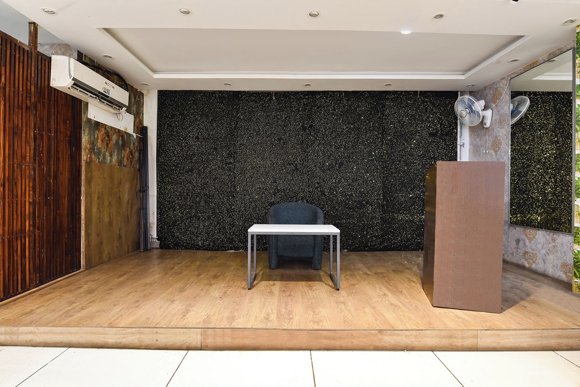 Una habitación con piso de madera, una mesa blanca, una pared con motas negras y una puerta de madera.