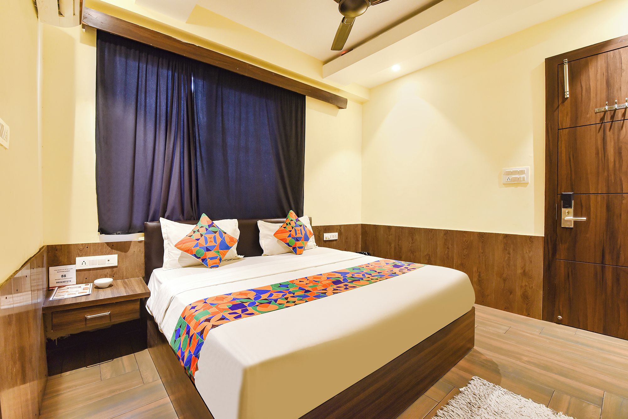 A hotel room with a bed, a nightstand, a wooden door, and a ceiling fan.