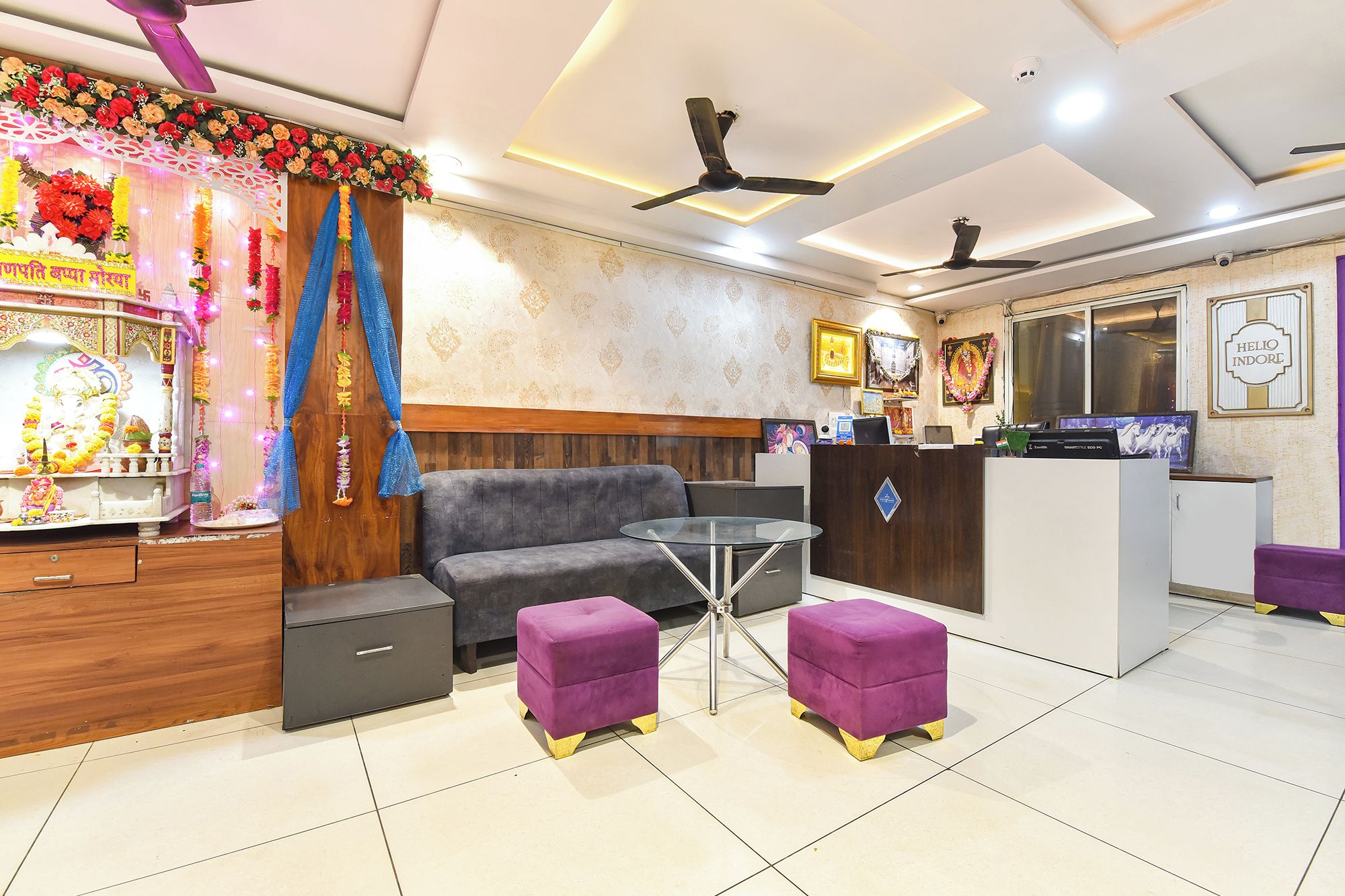 A hotel reception area with a sofa, purple ottomans, a glass table, and a reception desk.