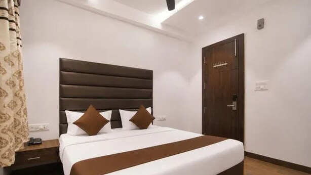 A hotel room with a large bed, a wooden door, and a nightstand. - Fabhotel Rudraksh Inn (Indore)