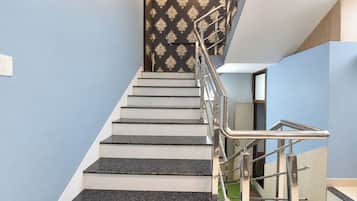 Una escalera con barandilla de metal, peldaños blancos y un papel tapiz estampado.