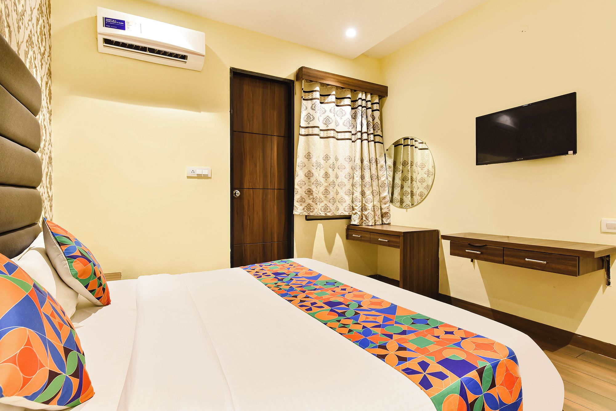 A hotel room with a bed, a TV, a wardrobe, and an air conditioning unit.