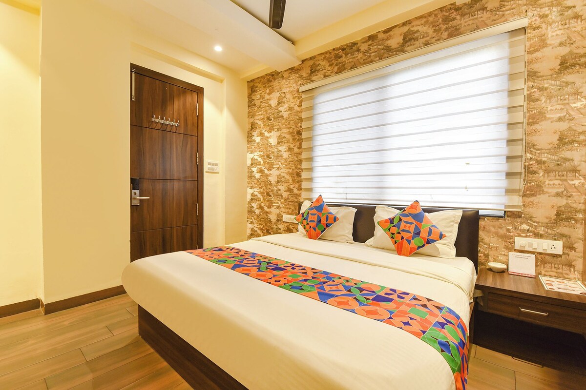Una habitación de hotel con una cama, una puerta de madera, una ventana con persianas y una pared con papel tapiz estampado.
