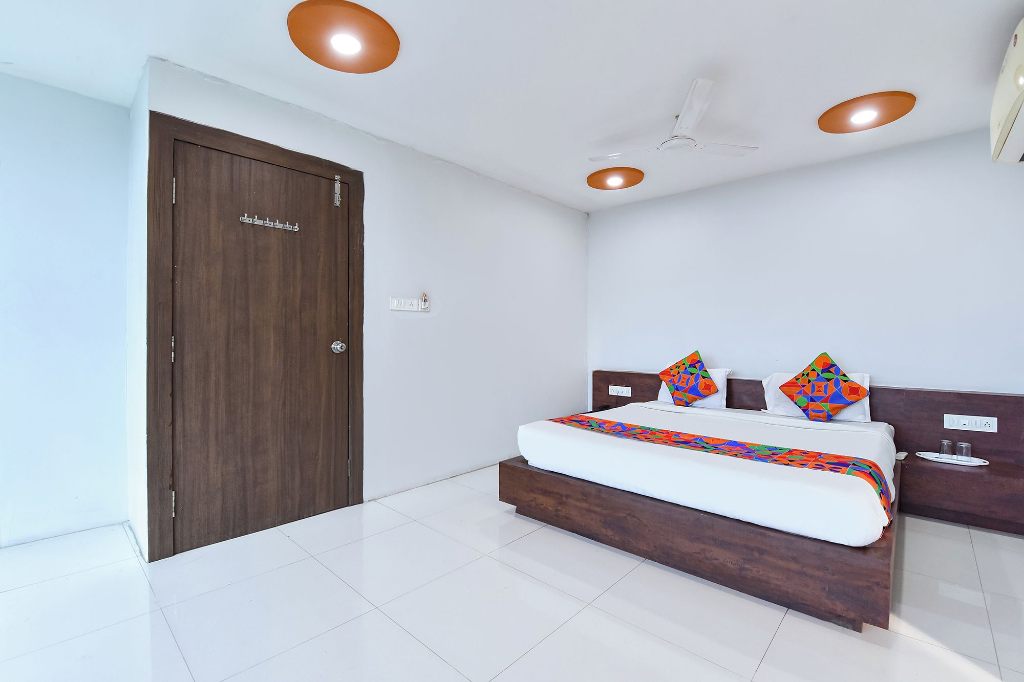 A bedroom with a bed, a wooden door, a ceiling fan, and recessed lighting.