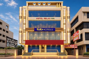 A modern hotel building with a prominent 'HOTEL RELAX INN' sign, a 'fabHOTELS' logo, and a reception area with a blue door.