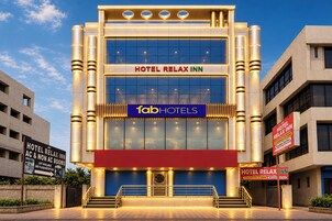 Un moderno edificio de hotel con un llamativo letrero que dice 'HOTEL RELAX INN', el logotipo de 'fabHOTELS' y una zona de recepción con una puerta azul.