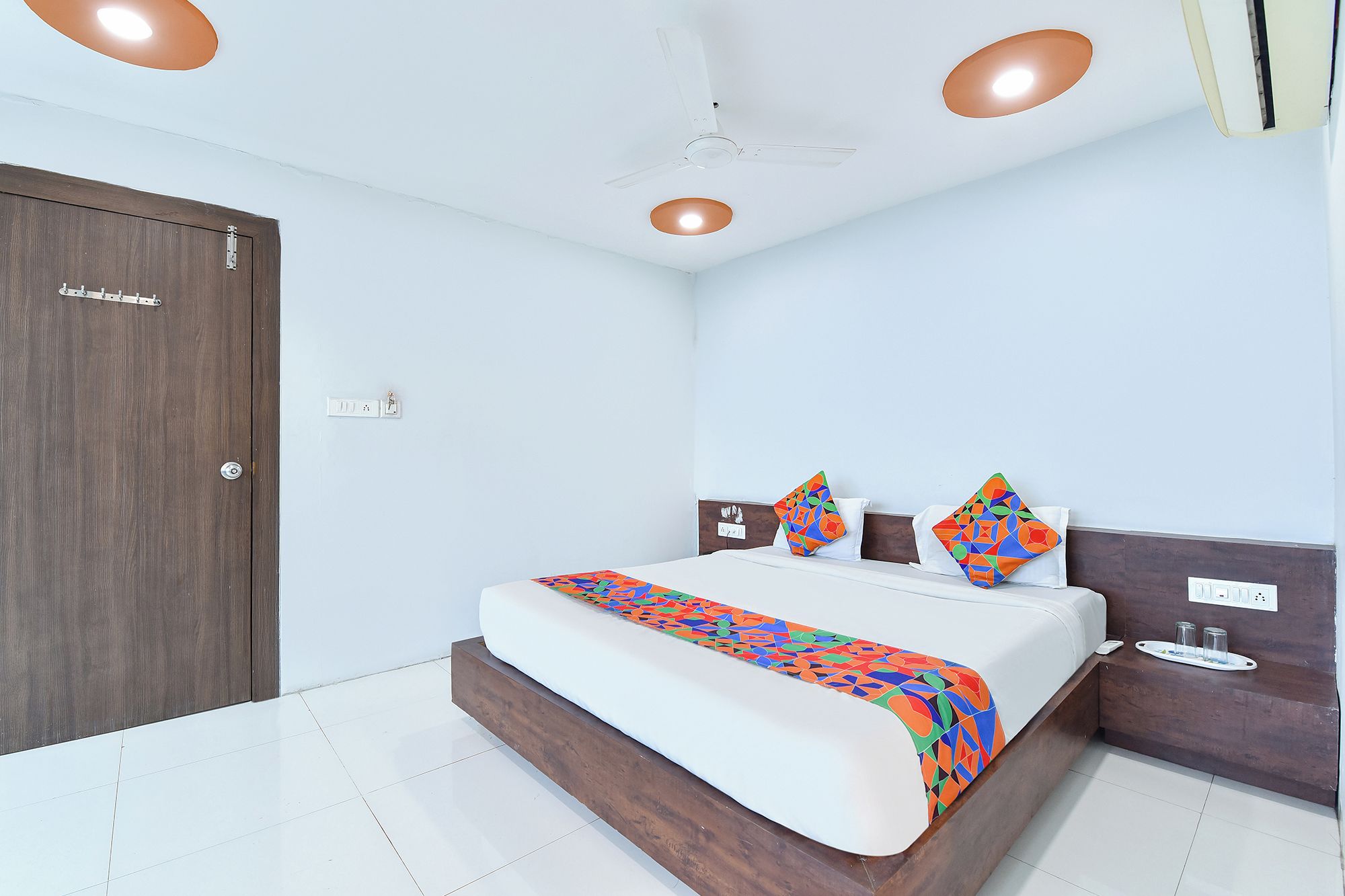 A bedroom with a bed, bedside table, nightstand, ceiling fan, and a door.