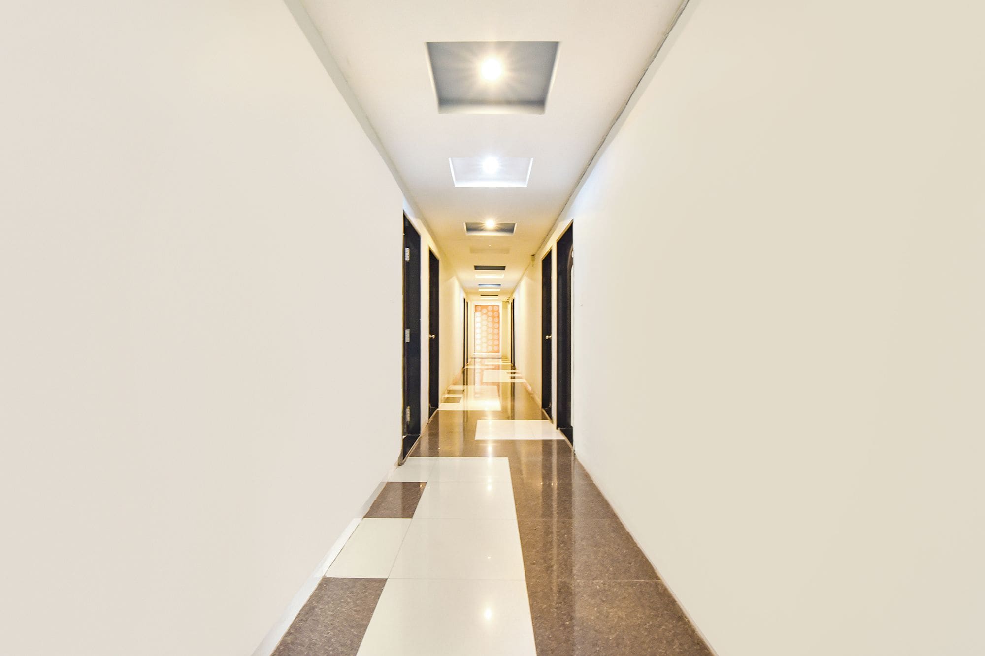 Un largo y estrecho pasillo de hotel con piso reflectante, iluminación empotrada y puertas a ambos lados.