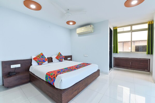 A modern hotel room with a large bed, bedside tables, a built-in wardrobe, an air conditioning unit, and a window with curtains.