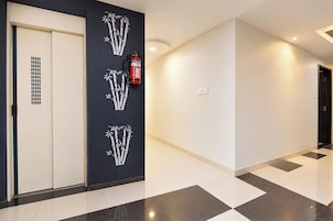 A hallway with a fire extinguisher mounted on the wall, a door with a vent, and a patterned floor.