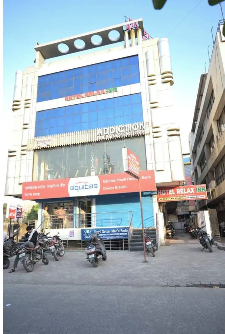 A multi-story building with a large glass facade, a visible sign for Equitas Small Finance Bank, and several parked motorcycles in front.