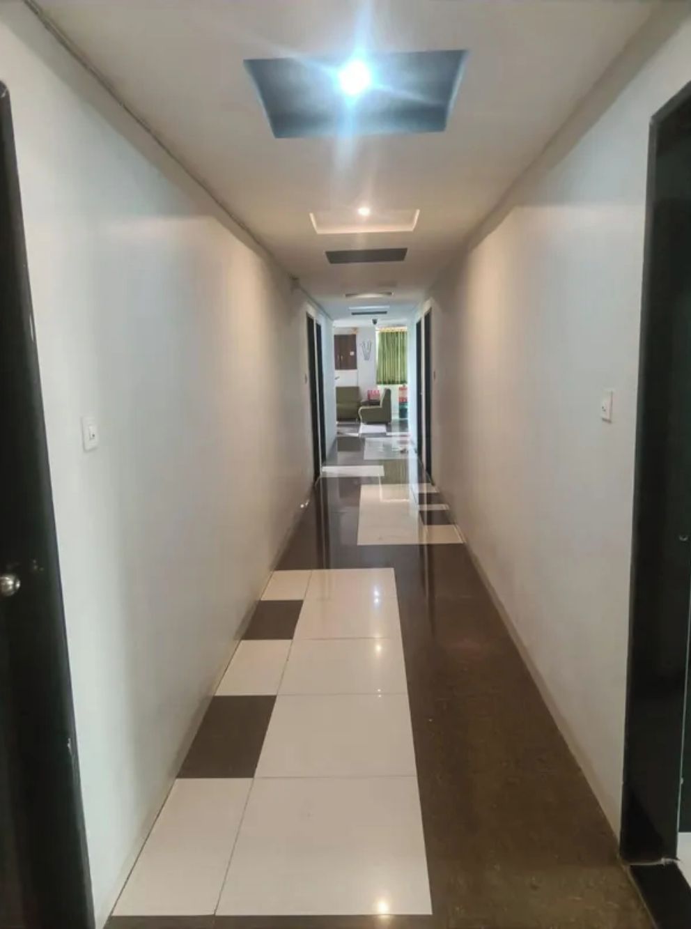 A corridor with a checkered floor pattern, leading to a room with a green curtain.