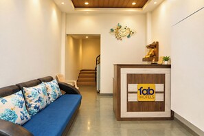A hotel reception area with a blue sofa, a wooden reception desk, and a clock on the wall. - FabHotel Jaihind Building (Pune)