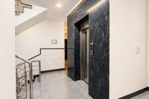 Un ascensor moderno con pantalla digital, pared de mármol y escalera de metal.