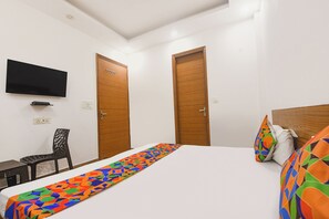 Habitación de hotel con cama, televisión montada en la pared, dos puertas de madera, una silla y un corredor de cama colorido.