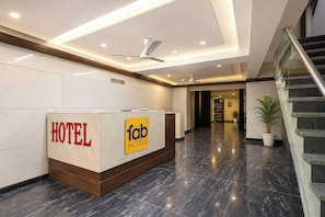 Zona de recepción de un hotel con mostrador, señalización indicativa y una escalera hacia otro piso.