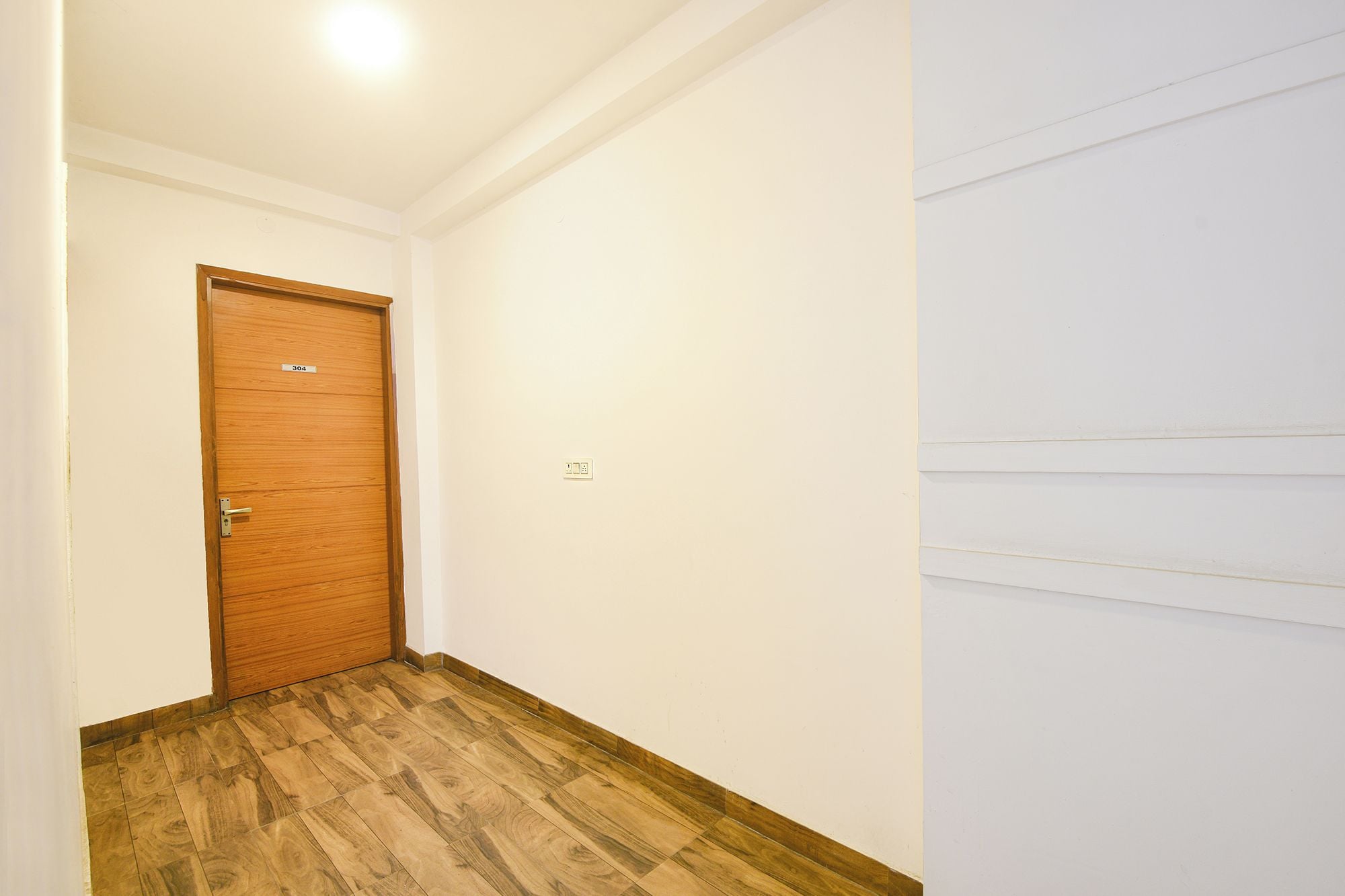 A hallway with a wooden door, white walls, and a wooden floor.