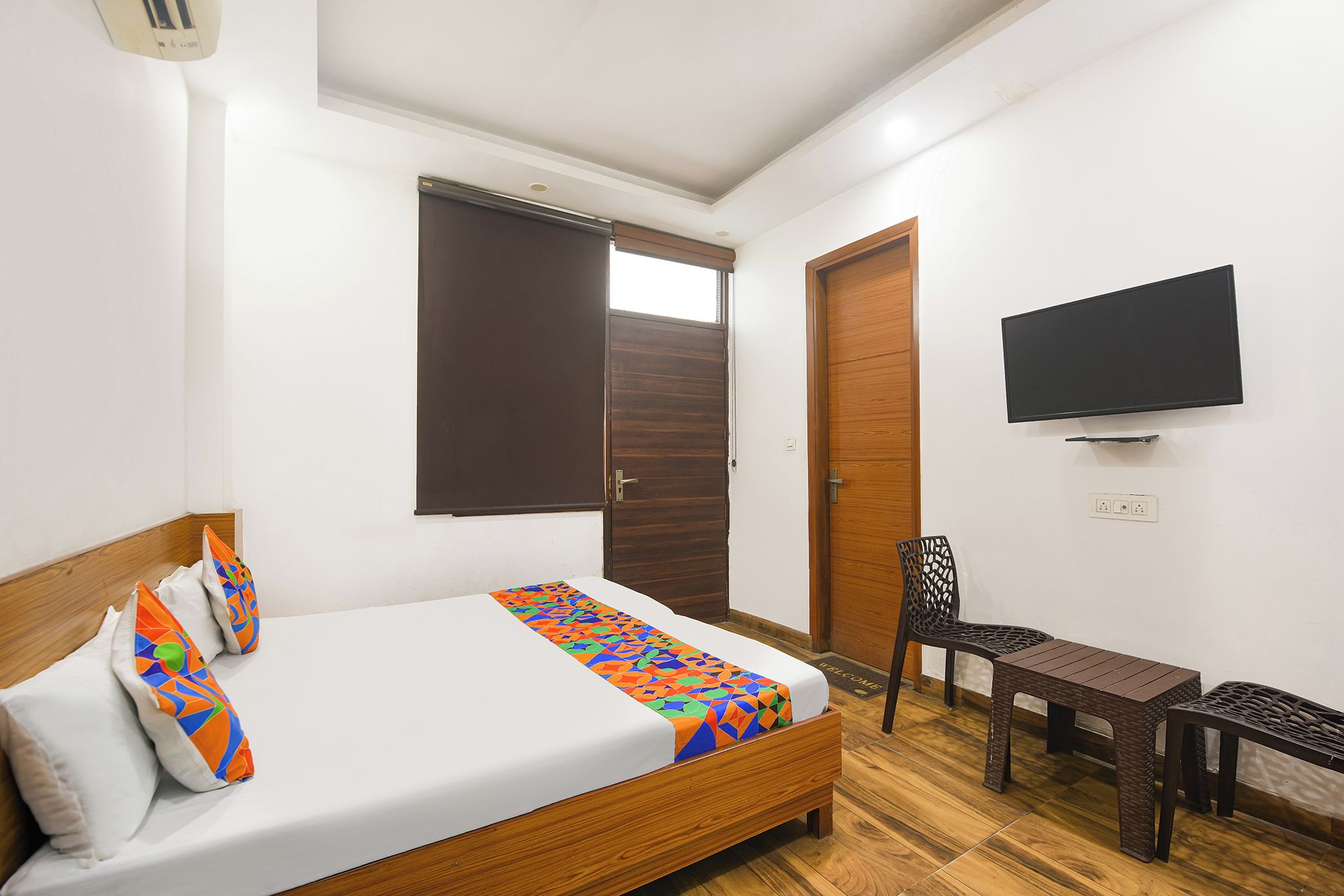 A hotel room with a bed, a TV mounted on the wall, a wooden door, and a small table.