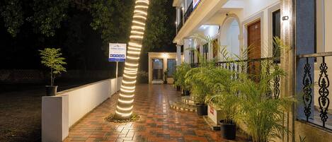 A hotel entrance with a brick pathway, potted plants, and a sign indicating amenities.