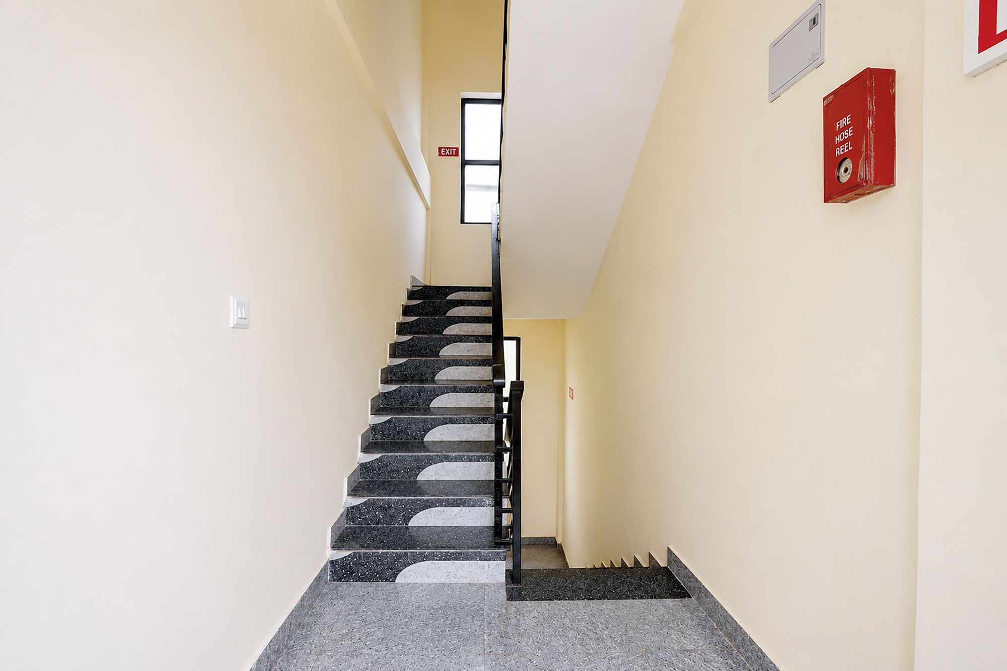 A stairway with a fire hose reel and an exit sign.