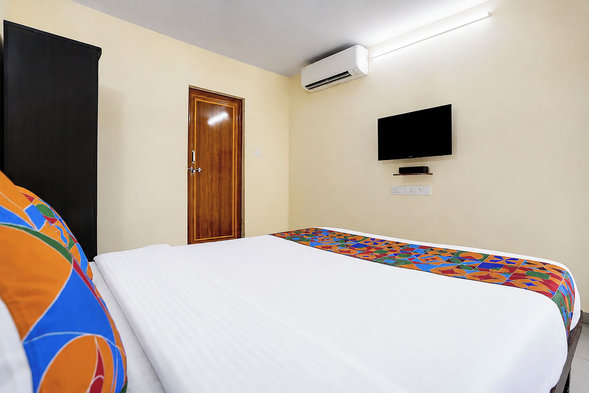 A hotel room with a bed, a television, an air conditioning unit, and a door.