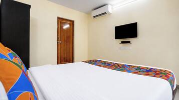 A hotel room with a bed, a television, an air conditioning unit, and a door.