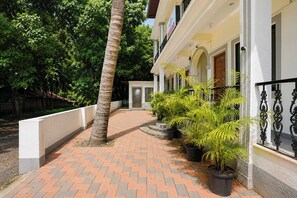 Un camino pavimentado que conduce a un edificio con fachada blanca, barandillas de hierro negro y plantas en macetas.