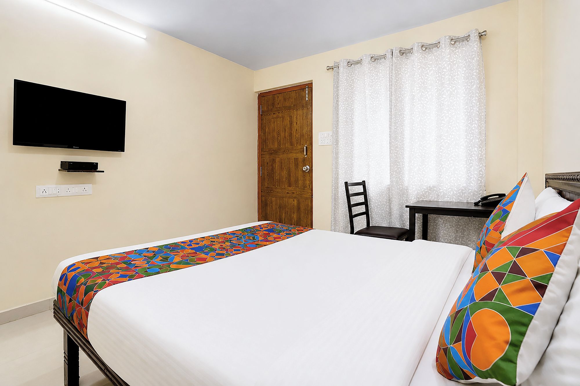 Una habitación de hotel con una cama, un escritorio, una silla, un televisor y una puerta.