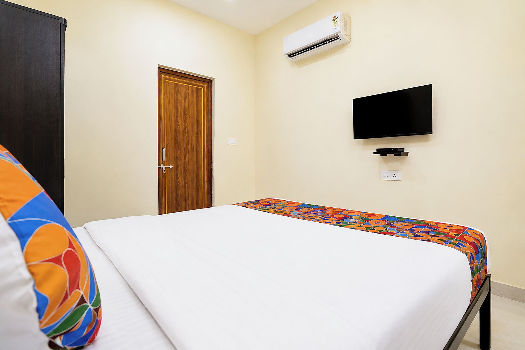 A bedroom with a bed, a television mounted on the wall, and an air conditioning unit.