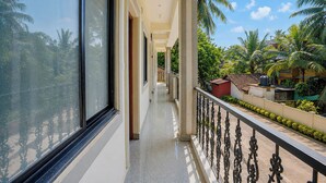 A corridor with a balcony overlooking a residential area with palm trees. - Fabhotel Avshree Crown Beach Stay (Calangute)