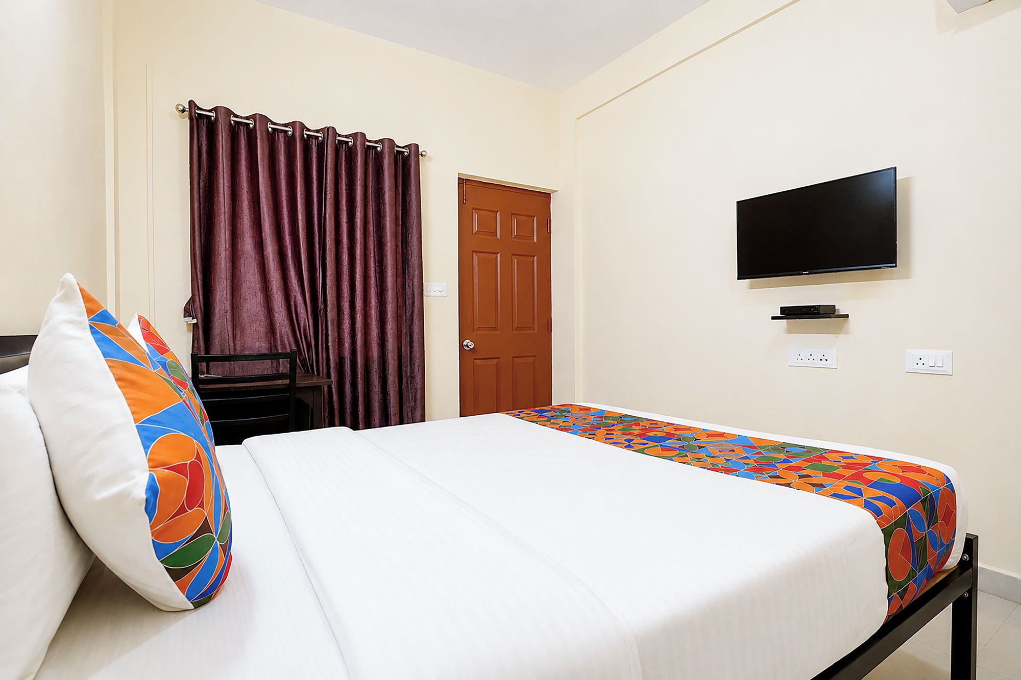Een hotelkamer met een bed, een aan de muur bevestigde televisie en een deur.