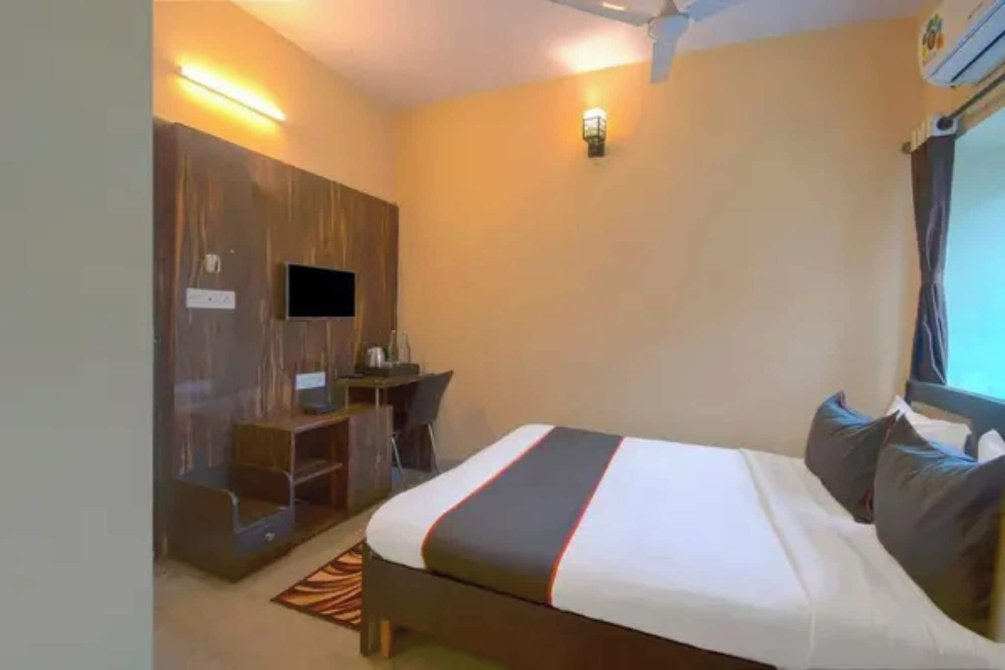 Una habitación de hotel con cama, escritorio, silla, televisor y ventilador de techo.