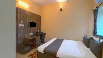 Una habitación de hotel con cama, escritorio, silla, televisor y ventilador de techo.