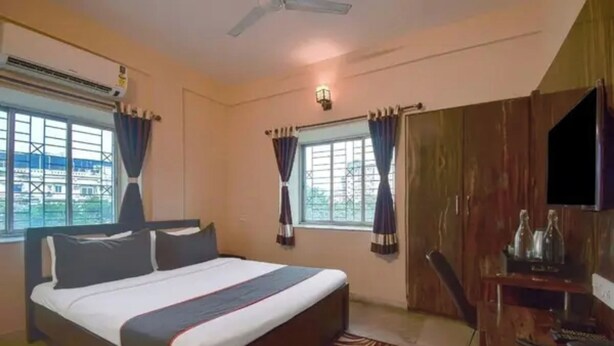 Un dormitorio con cama, ventilador de techo, televisión y ventana con cortinas.