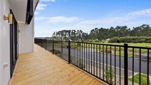 Ein Balkon mit Holzboden und schwarzer Metallreling, mit Blick auf eine Straße und Grünflächen.