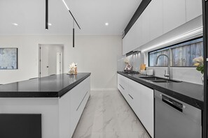 A modern kitchen with a central island, white cabinetry, and a built-in dishwasher.