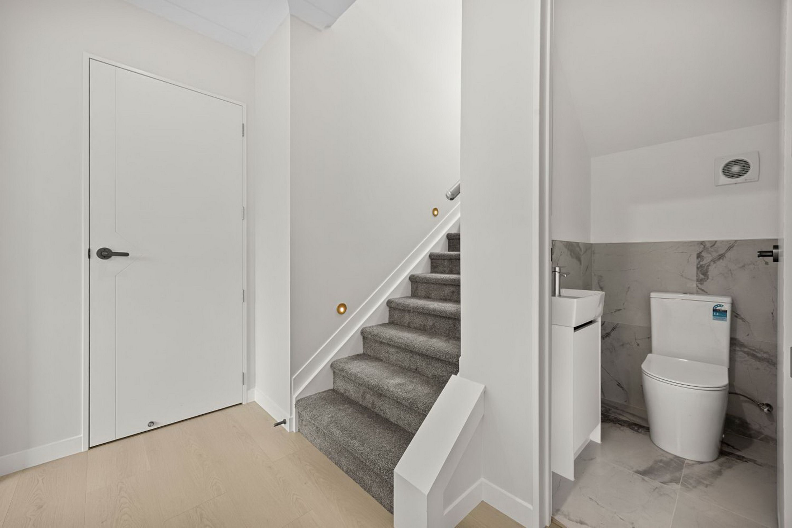 Un interior moderno con una puerta blanca, una escalera con alfombra y un baño con inodoro y lavabo.