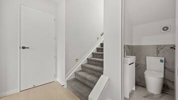 Un interior moderno con una puerta blanca, una escalera con alfombra y un baño con inodoro y lavabo.